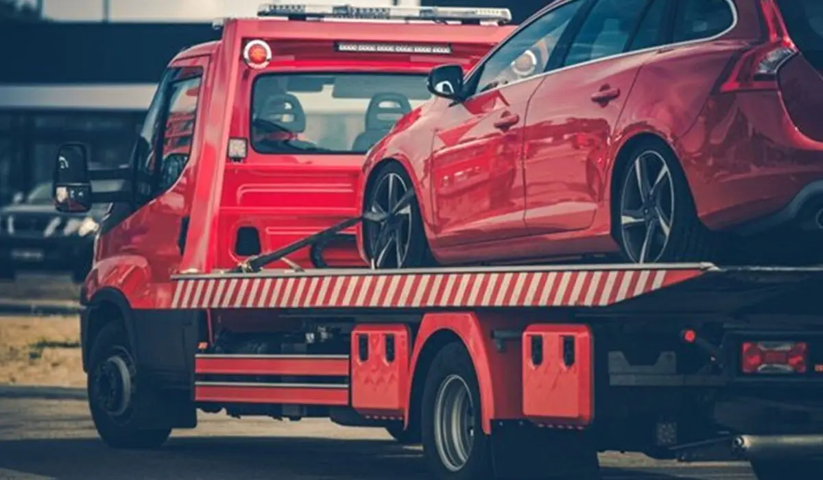 a small red car being towed away by a large red truck