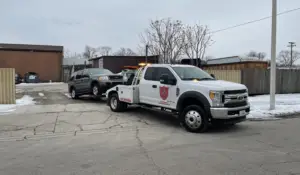 Small junk auto getting towed by white truck.