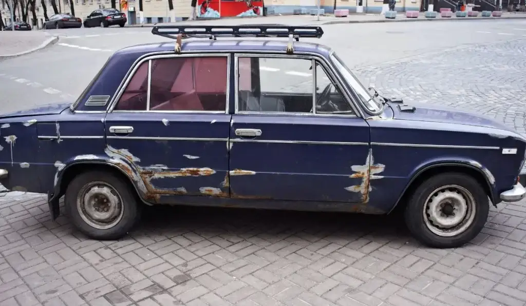 Old, rusted junk car parked on city street ready for sale or removal.