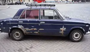 Old, rusted junk car parked on city street ready for sale or removal.