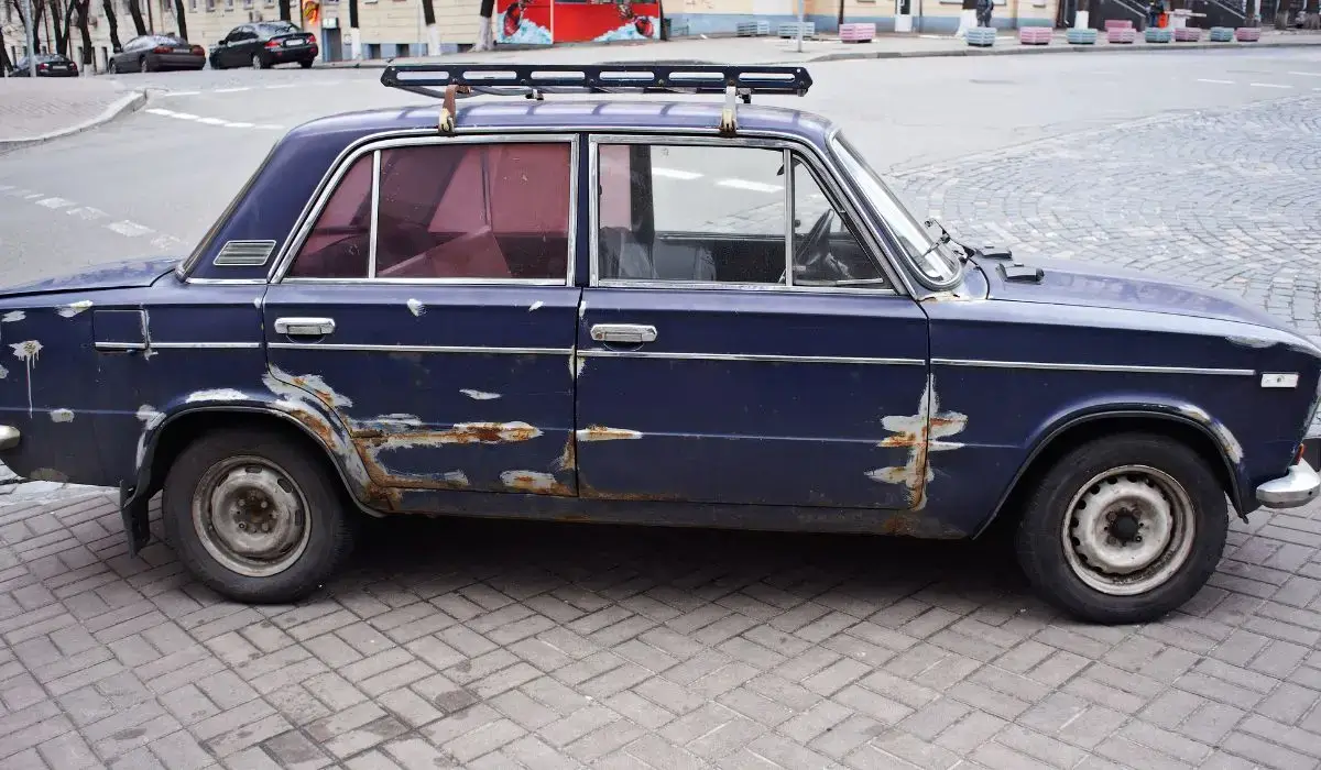 Old, rusted junk car parked on city street ready for sale or removal.