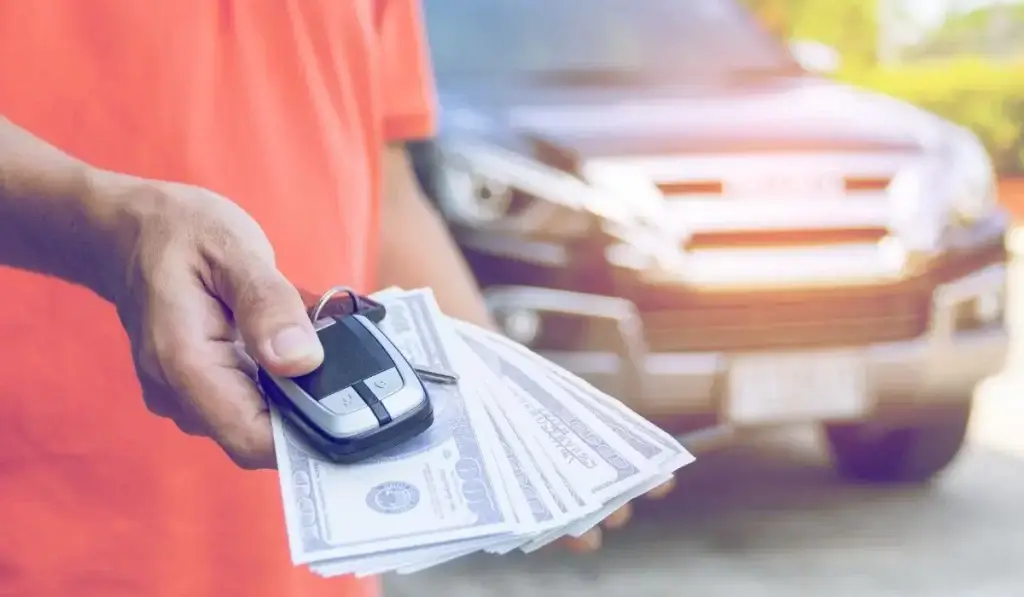 Person handing over car keys and receiving cash for a financed car sale through A+ Junk N Tow.