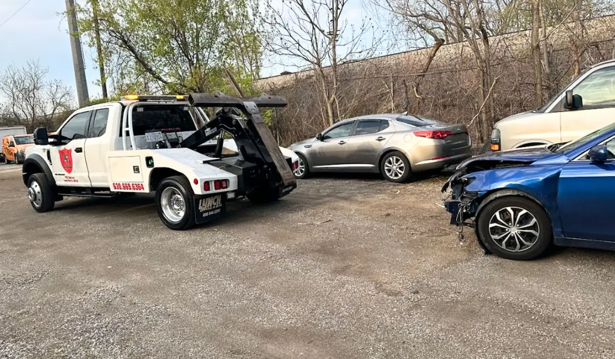 Tow truck preparing to legally remove an abandoned car from a gravel lot in Illinois during daylight.