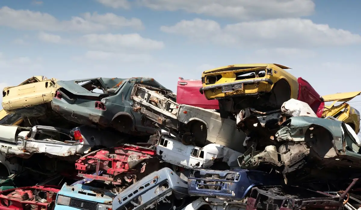 Crumpled junk cars piled high in a recycling yard, showing the final stage of auto metal recovery process.