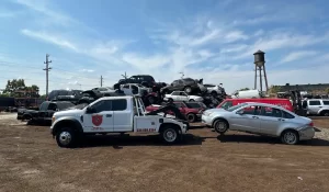 Tow truck removing a junk vehicle at an Illinois scrap yard with stacked cars in the background.
