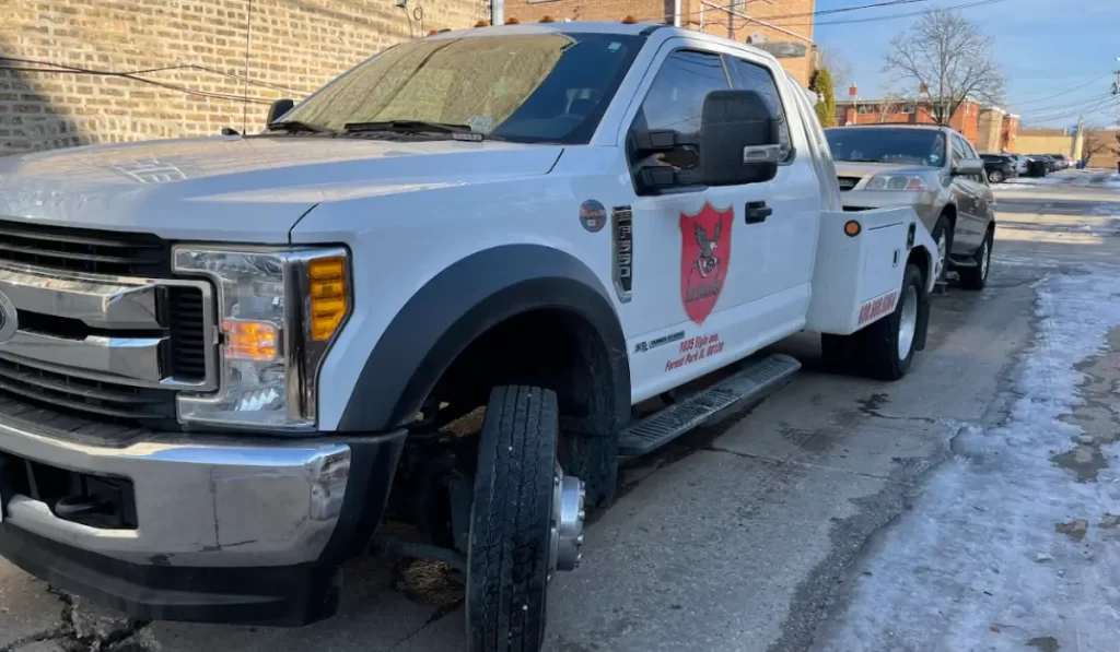 Tow truck performing eco-friendly junk car removal on Illinois street with a vehicle safely loaded for transport.