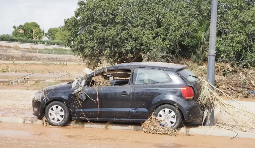 Flood-damaged black car abandoned roadside with debris and broken windows, shown as a candidate to sell flooded car