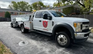 Wheel-lift tow truck removing a collision-damaged sedan in an Illinois neighborhood, illustrating the junk car value process.