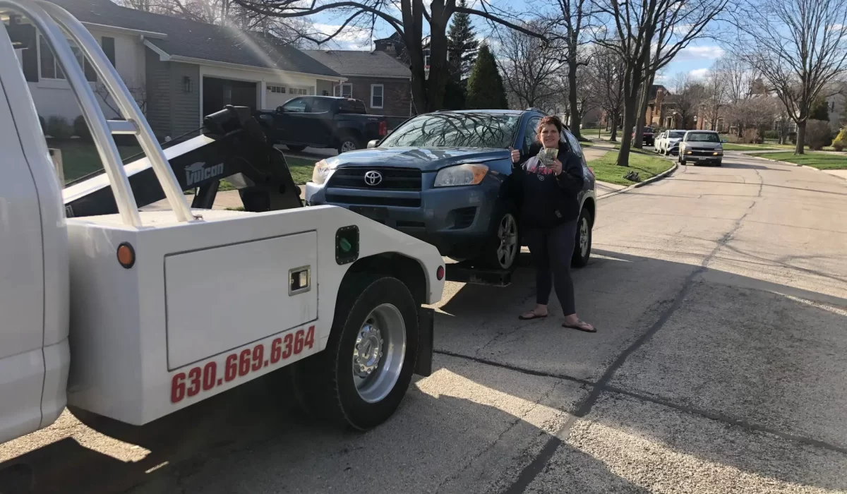 Cash for Junk Cars Near Me Tow truck hauling away vehicle as woman evaluates junk car value vs. trade-in for more money.